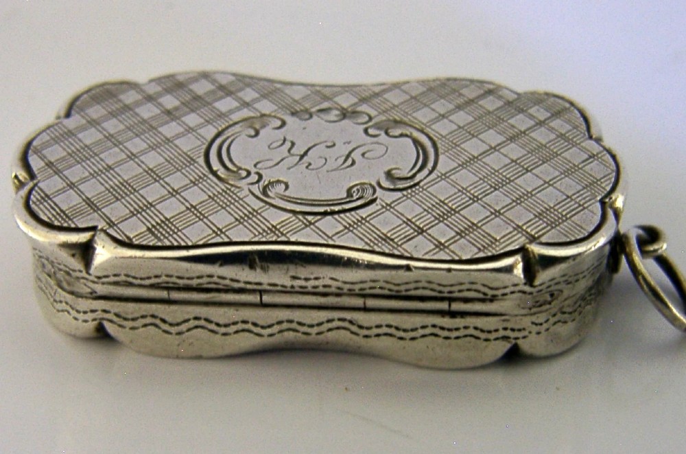 An antique Victorian sterling silver vinaigrette box featuring a shaped lobed outline, engine-turned geometric engraving, and a central engraved monogram cartouche. View VIII