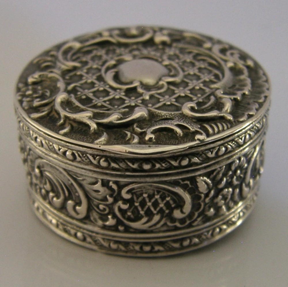 A circular French solid silver pill box with Rococo Revival lattice and floral scroll embossing. View IV