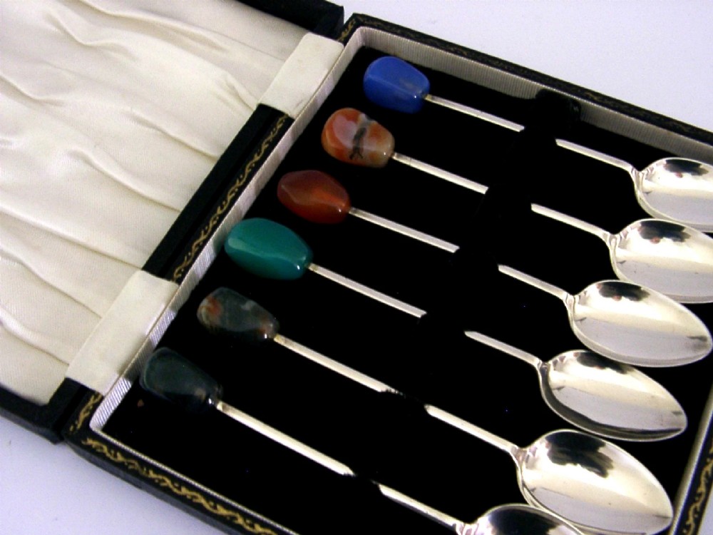 A cased set of six sterling silver coffee spoons with assorted colourful polished agate finials arranged in a dark lined presentation box. View II