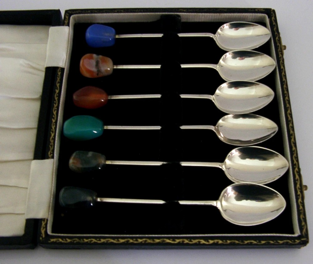 A cased set of six sterling silver coffee spoons with assorted colourful polished agate finials arranged in a dark lined presentation box. View IV