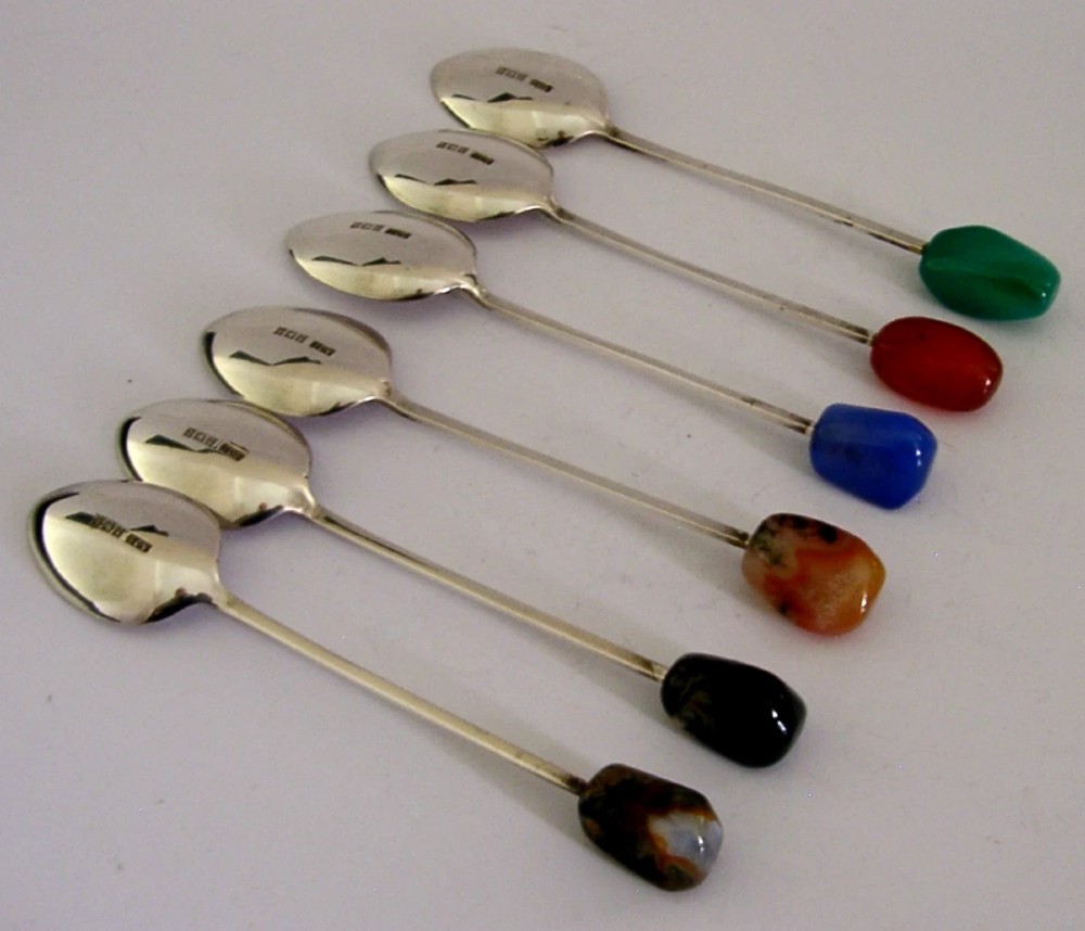 A cased set of six sterling silver coffee spoons with assorted colourful polished agate finials arranged in a dark lined presentation box. View VII