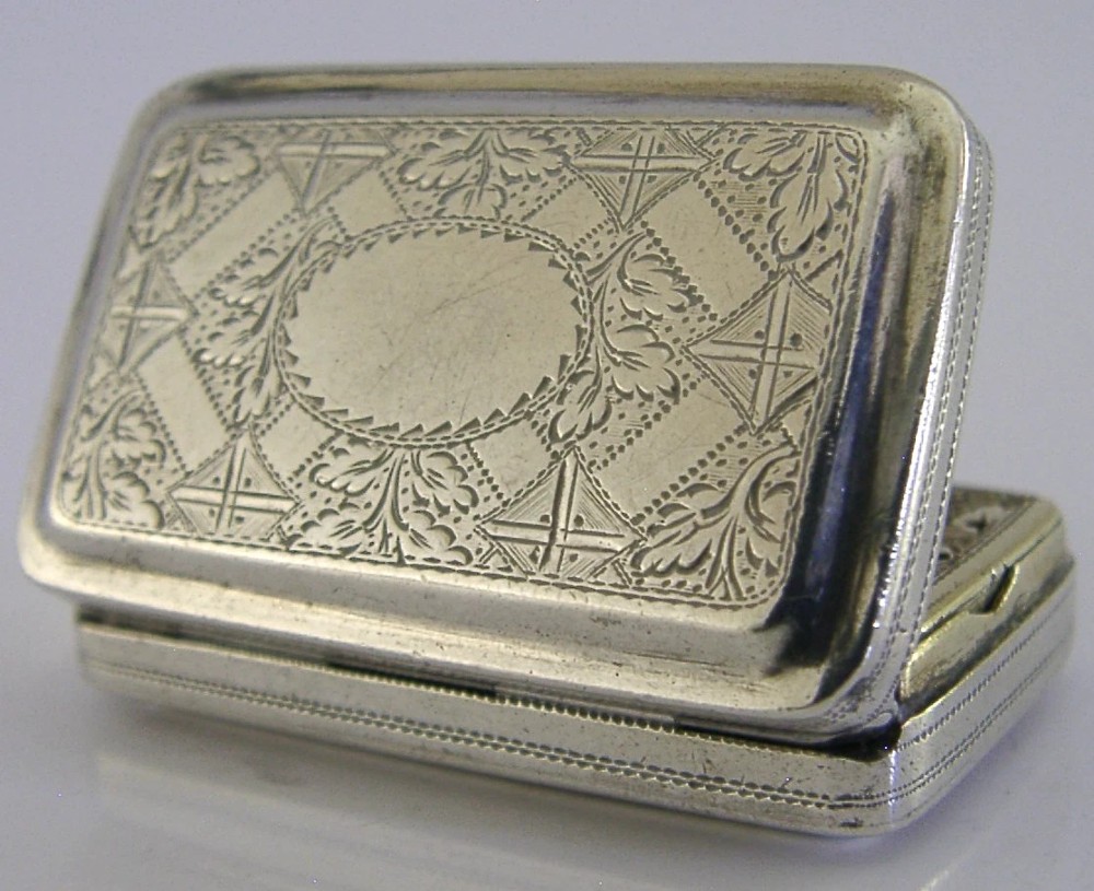 An open rectangular Georgian sterling silver vinaigrette box displaying an engraved exterior and a pierced gold-gilded inner grille featuring floral leaf patterns. View IX