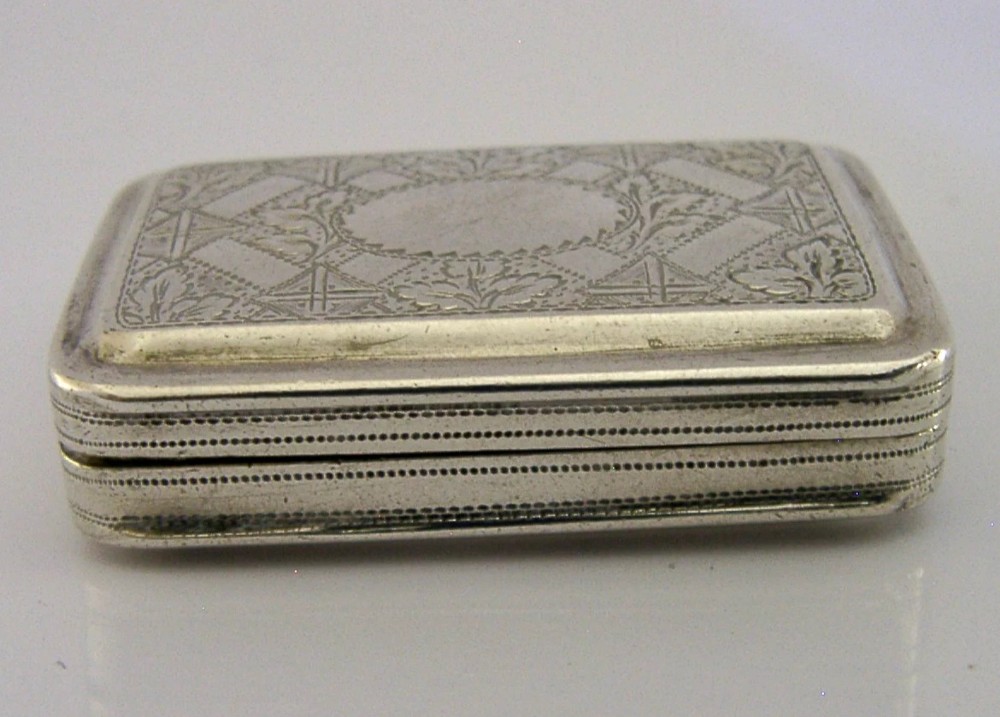 An open rectangular Georgian sterling silver vinaigrette box displaying an engraved exterior and a pierced gold-gilded inner grille featuring floral leaf patterns. View X