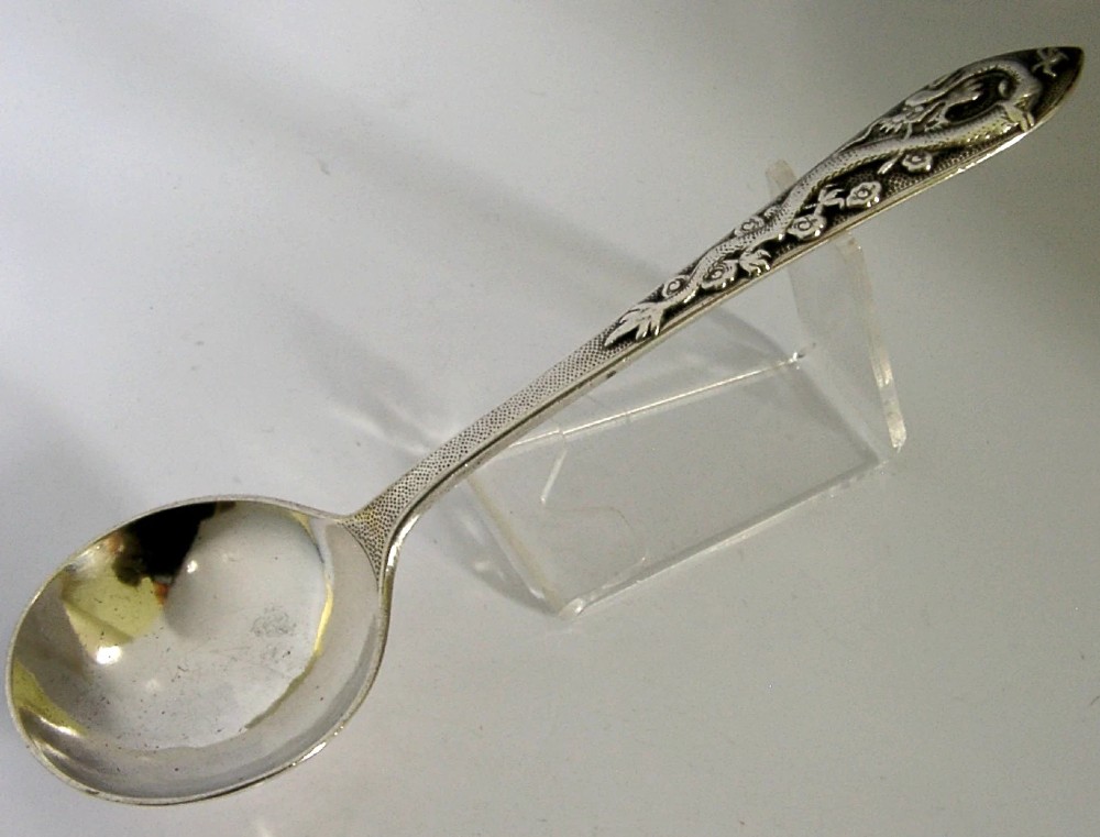 An antique silver serving ladle featuring a rounded circular bowl and a detailed dragon relief chased along the handle.