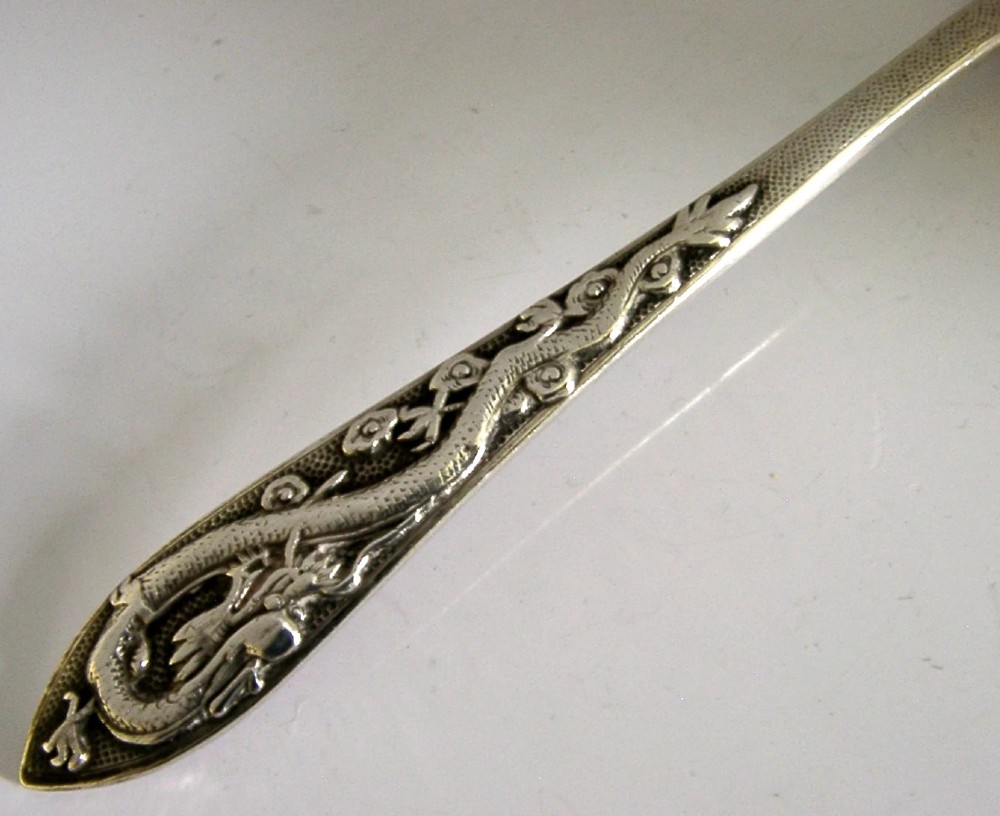 An antique silver serving ladle featuring a rounded circular bowl and a detailed dragon relief chased along the handle. View V