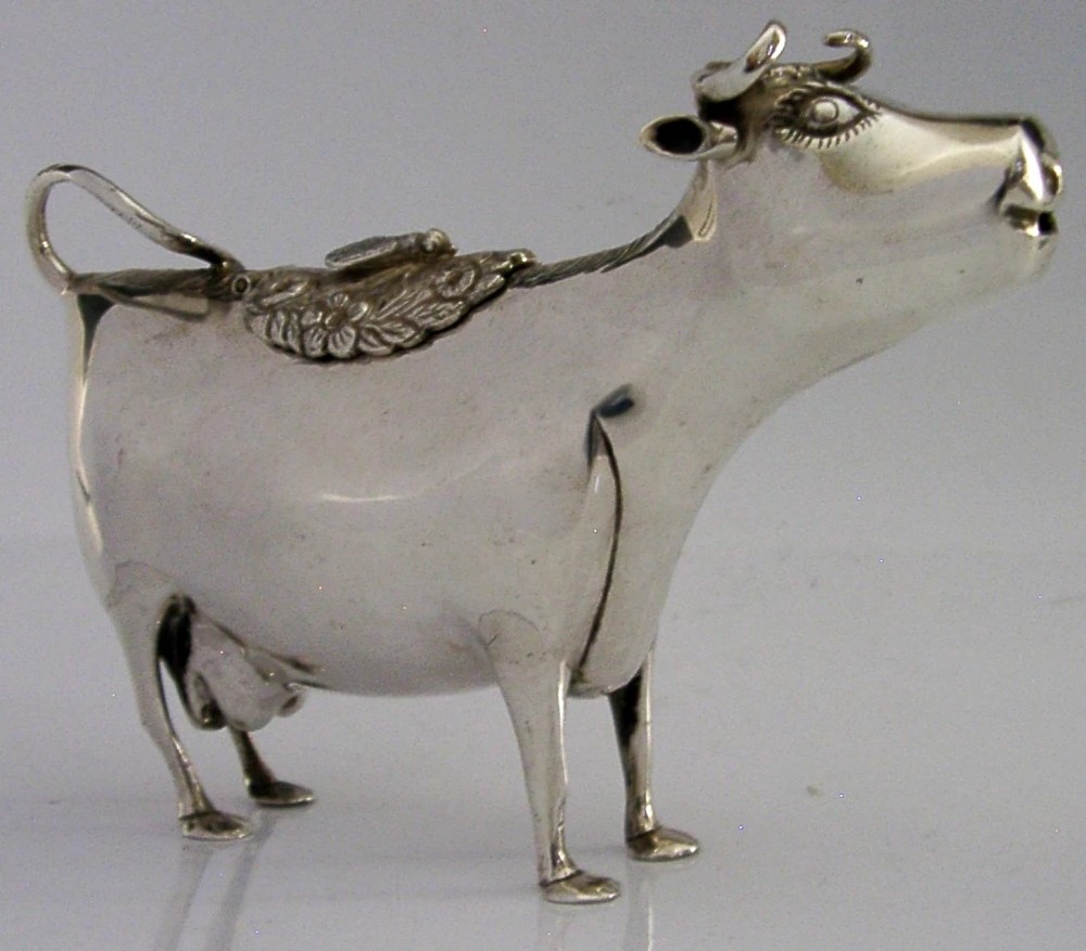 A sterling silver novelty cow creamer featuring a hollow cast body, a hinged lid decorated with floral motifs on the back, and a looped tail handle. View VI