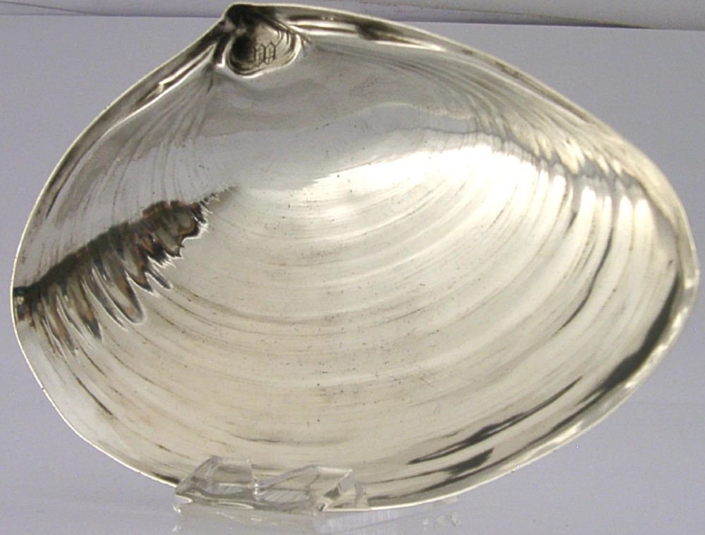 A sterling silver dish crafted in the shape of an open clam shell with visible concentric ridged textures and polished metallic surface. View II