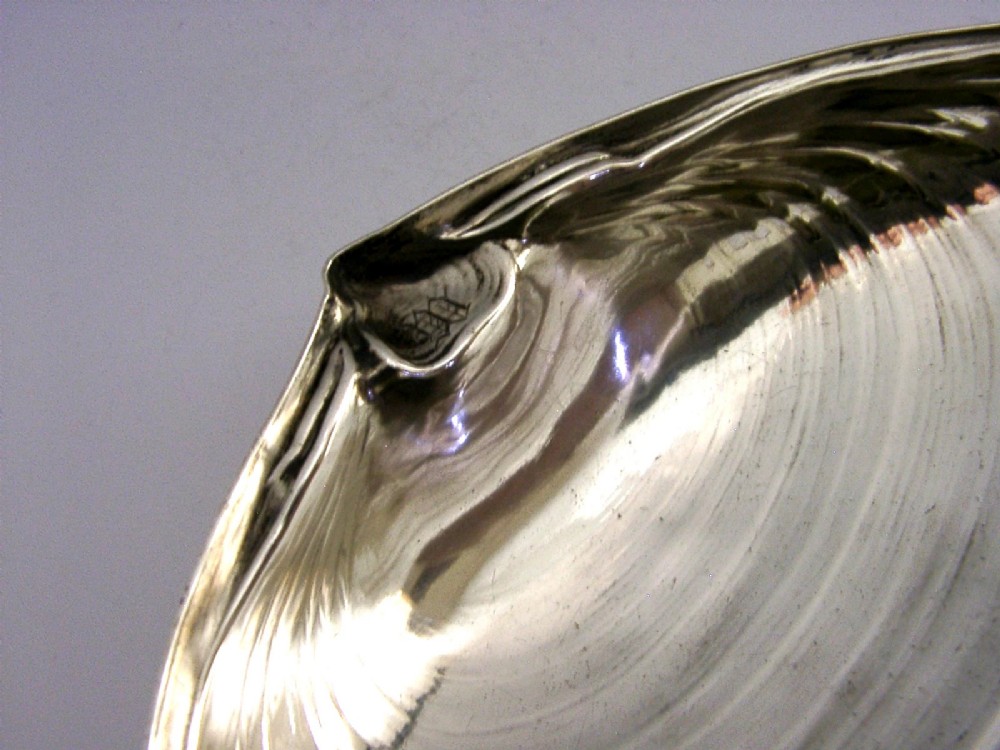 A sterling silver dish crafted in the shape of an open clam shell with visible concentric ridged textures and polished metallic surface. View III
