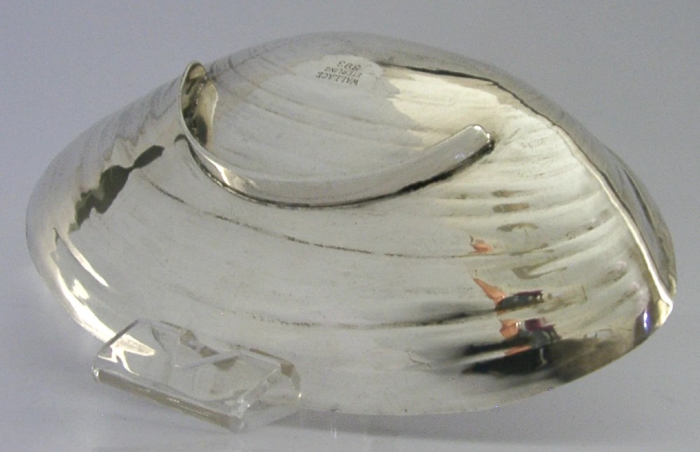 A sterling silver dish crafted in the shape of an open clam shell with visible concentric ridged textures and polished metallic surface. View V