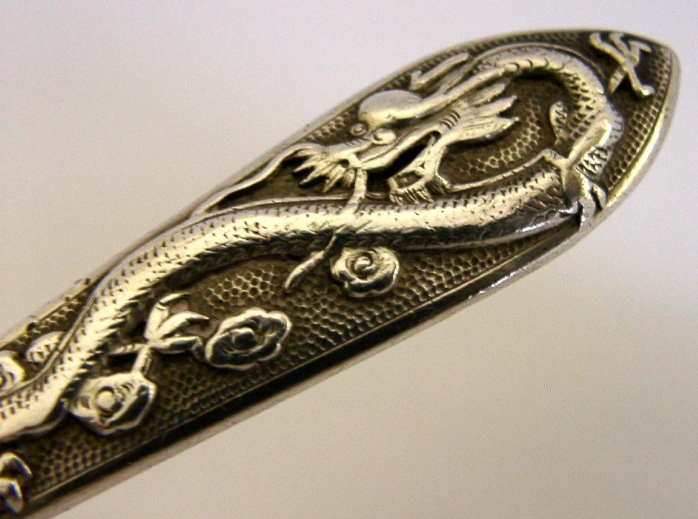An antique Chinese export silver spoon featuring a detailed chased dragon design sculpted along its handle and a polished oval bowl. View II
