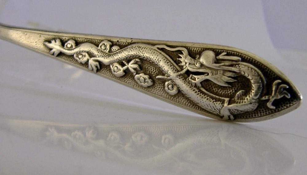 An antique Chinese export silver spoon featuring a detailed chased dragon design sculpted along its handle and a polished oval bowl. View V