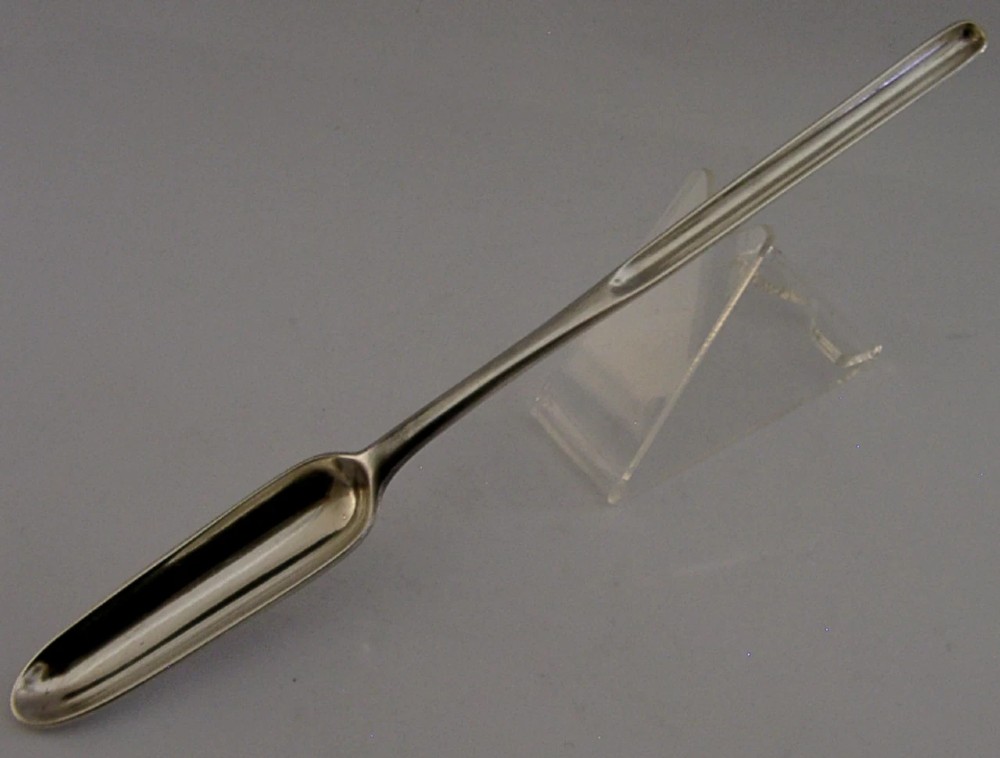 A Georgian sterling silver marrow scoop featuring an engraved family crest on the elongated scoop and stamped hallmarks along the narrow handle. View V