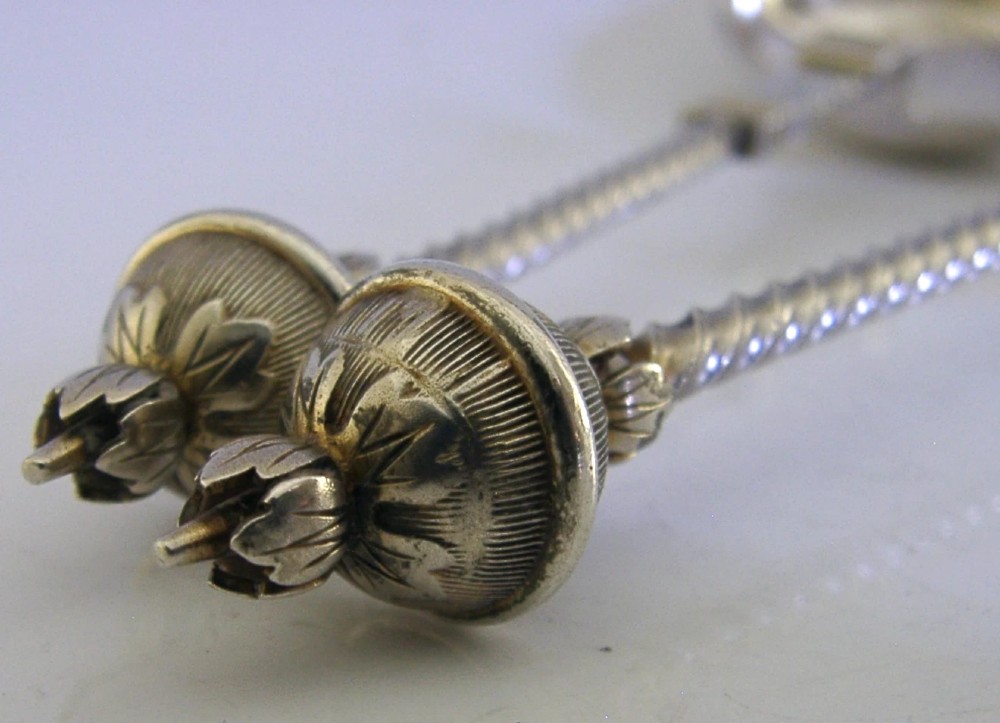 A pair of antique Norwegian silver serving spoons featuring round engraved bowls, twisted wire stems, and decorative knop finials. View VI