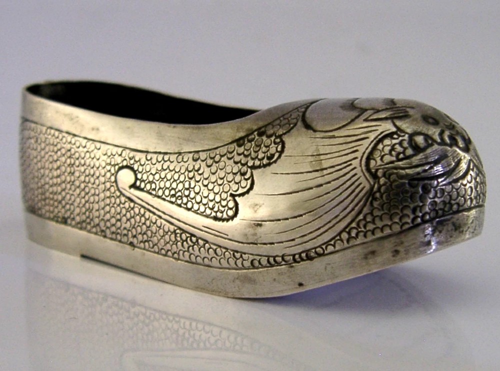 An antique Chinese export silver novelty pin cushion formed in the shape of a traditional slipper, featuring chased bat motifs and textured surface decoration.