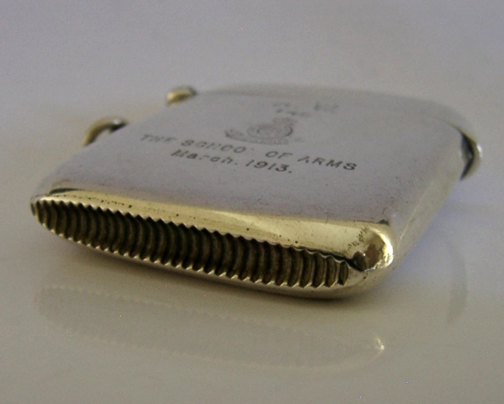 An Edwardian sterling silver vesta case featuring engraved military crests, text reading THE SCHOOL OF ARMS March. 1913, a side attachment ring, and a hinged lid. View V