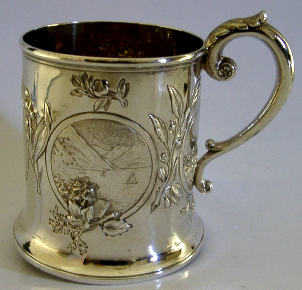 A Victorian sterling silver tankard mug featuring detailed relief floral decoration, a landscape roundel, a scroll handle, and a gilt interior. View III