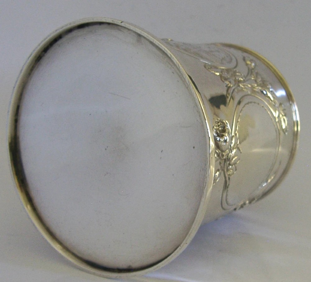 A Victorian sterling silver tankard mug featuring detailed relief floral decoration, a landscape roundel, a scroll handle, and a gilt interior. View XI