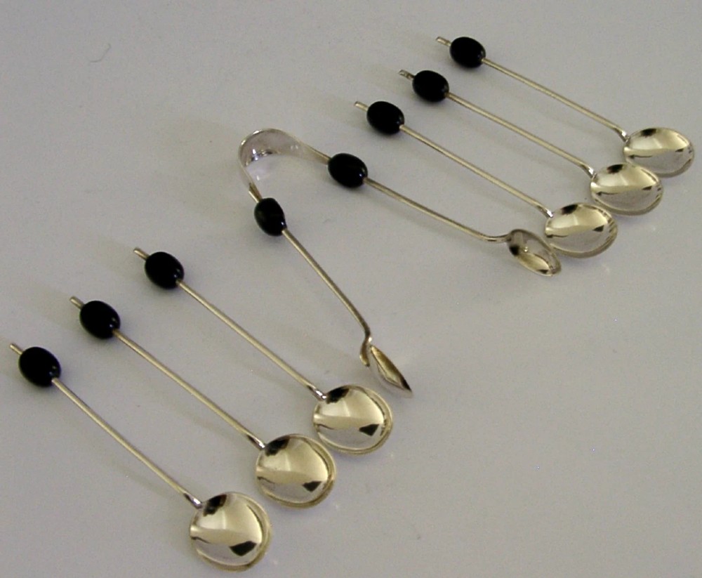 A fitted display case containing six sterling silver coffee spoons with black coffee bean finials and matching sugar tongs. View III