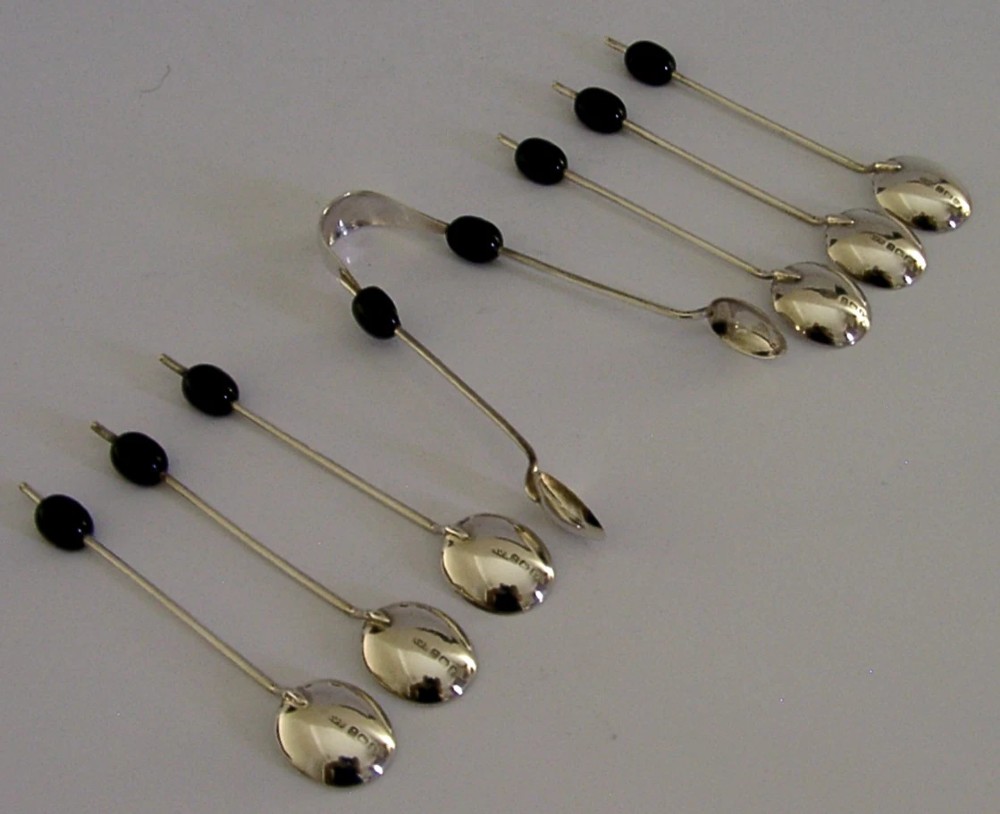 A fitted display case containing six sterling silver coffee spoons with black coffee bean finials and matching sugar tongs. View VII