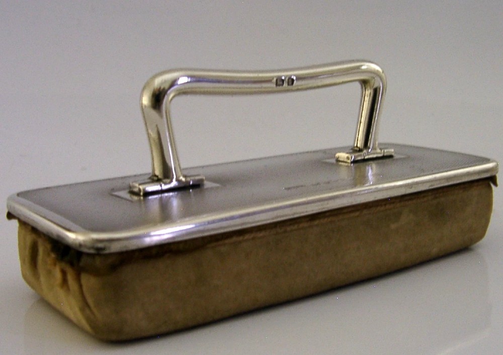An engine-turned sterling silver nail buffer featuring a folding rectangular handle and English hallmarks, resting on a chamois base. View III