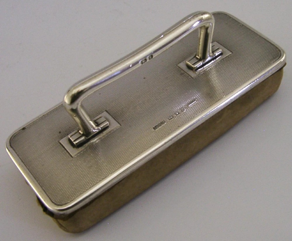 An engine-turned sterling silver nail buffer featuring a folding rectangular handle and English hallmarks, resting on a chamois base. View IV