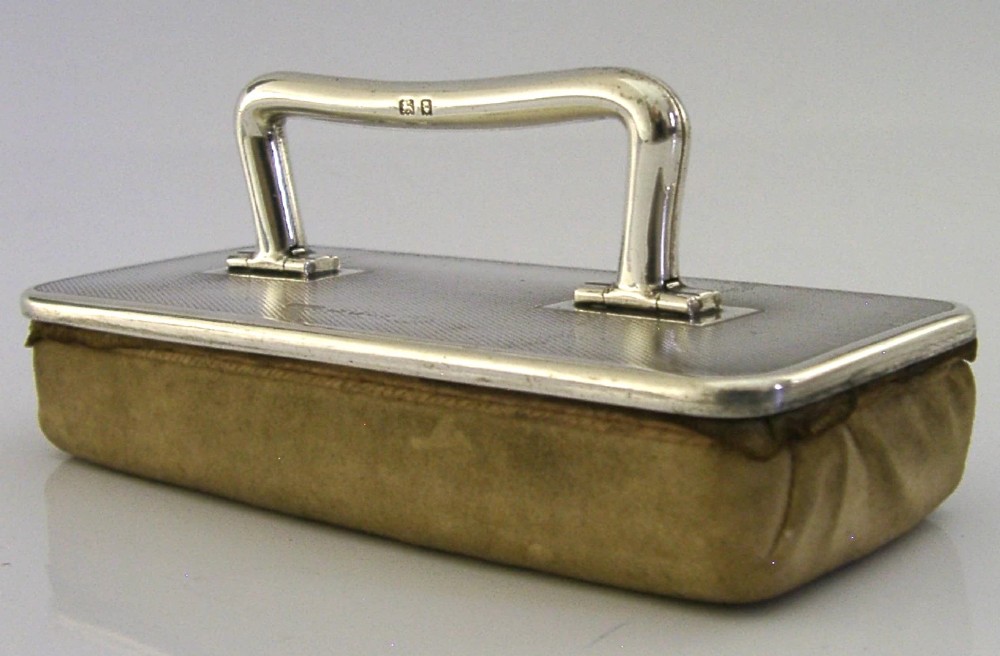 An engine-turned sterling silver nail buffer featuring a folding rectangular handle and English hallmarks, resting on a chamois base. View V