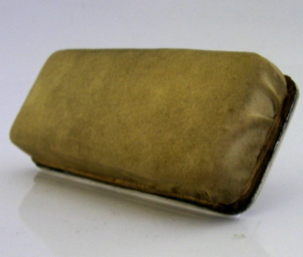 An engine-turned sterling silver nail buffer featuring a folding rectangular handle and English hallmarks, resting on a chamois base. View VI