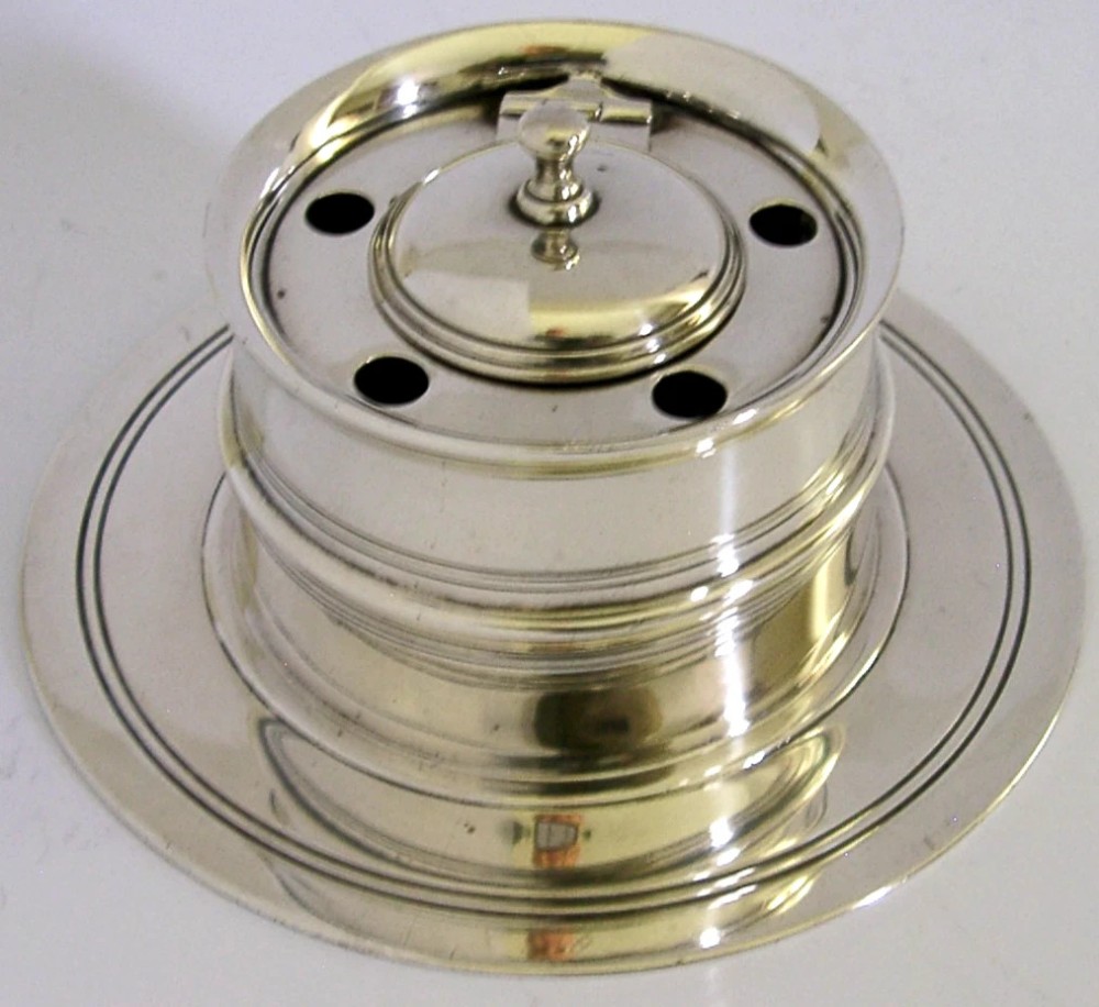 A solid sterling silver circular capstan inkwell featuring a hinged central lid and pierced quill holes set upon a wide dished base with visible hallmarks. View IV