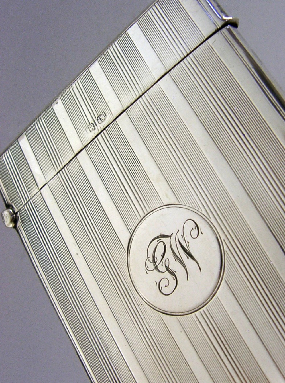 An open rectangular sterling silver card case with linear engine-turned patterns and a central circular monogrammed cartouche. View III