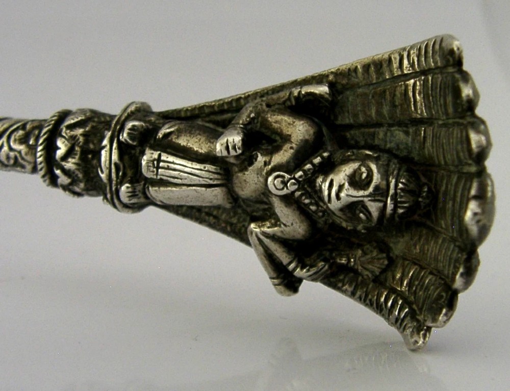 An antique silver offering spoon featuring a shell-shaped bowl, a decorated twisted stem, and a deity finial framed by a snake hood. View IV