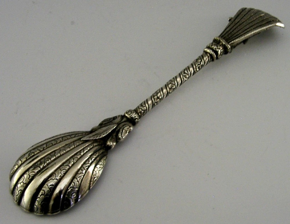 An antique silver offering spoon featuring a shell-shaped bowl, a decorated twisted stem, and a deity finial framed by a snake hood. View V