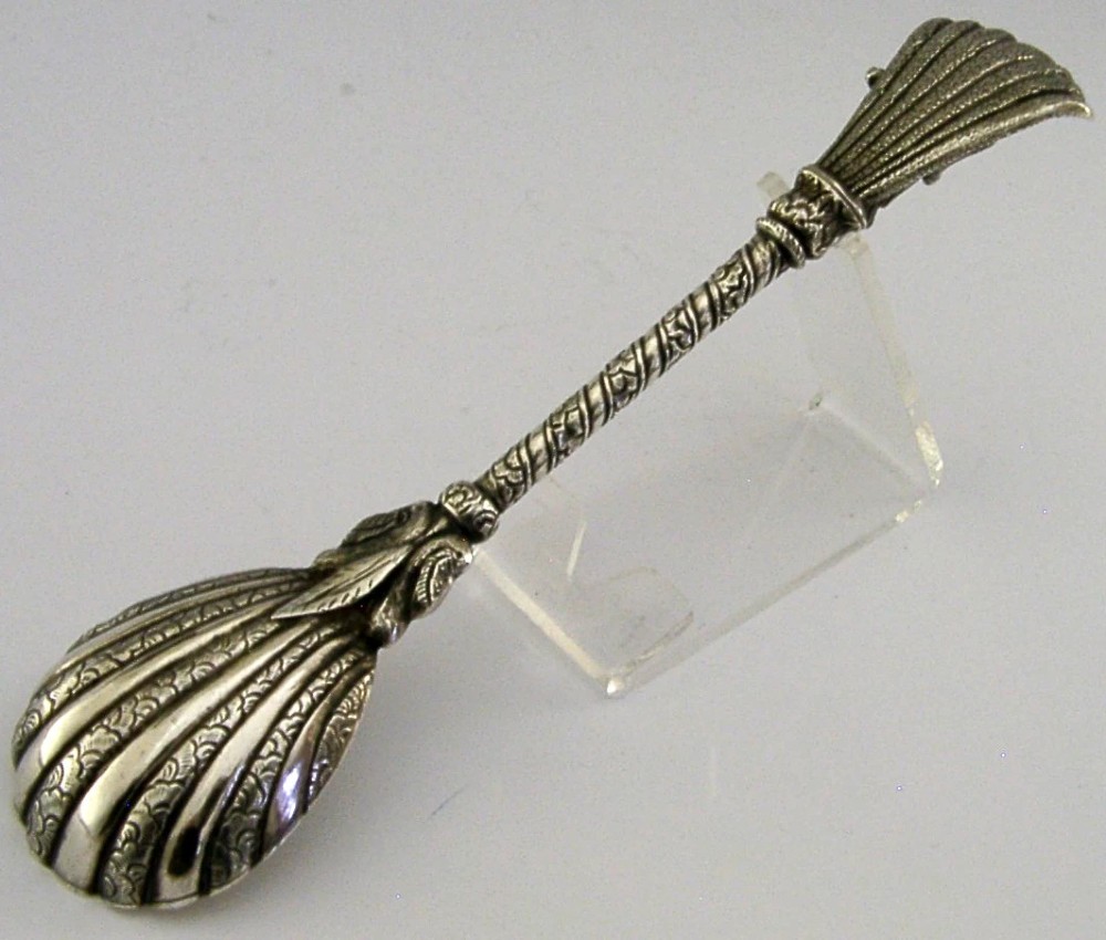 An antique silver offering spoon featuring a shell-shaped bowl, a decorated twisted stem, and a deity finial framed by a snake hood. View VII