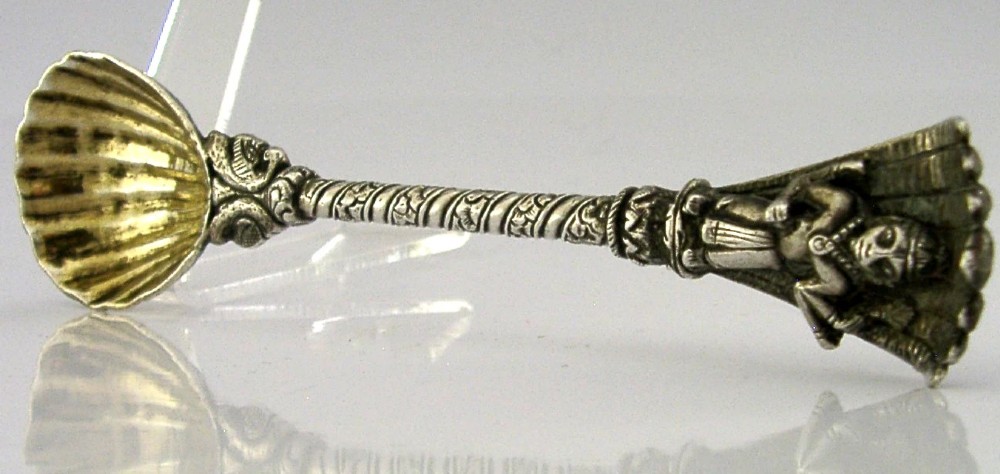 An antique silver offering spoon featuring a shell-shaped bowl, a decorated twisted stem, and a deity finial framed by a snake hood. View IX