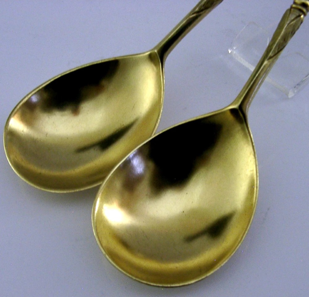 A pair of Victorian sterling silver gilt serving spoons featuring oval bowls and detailed cast handles with grotesque mask and scroll motifs. View V
