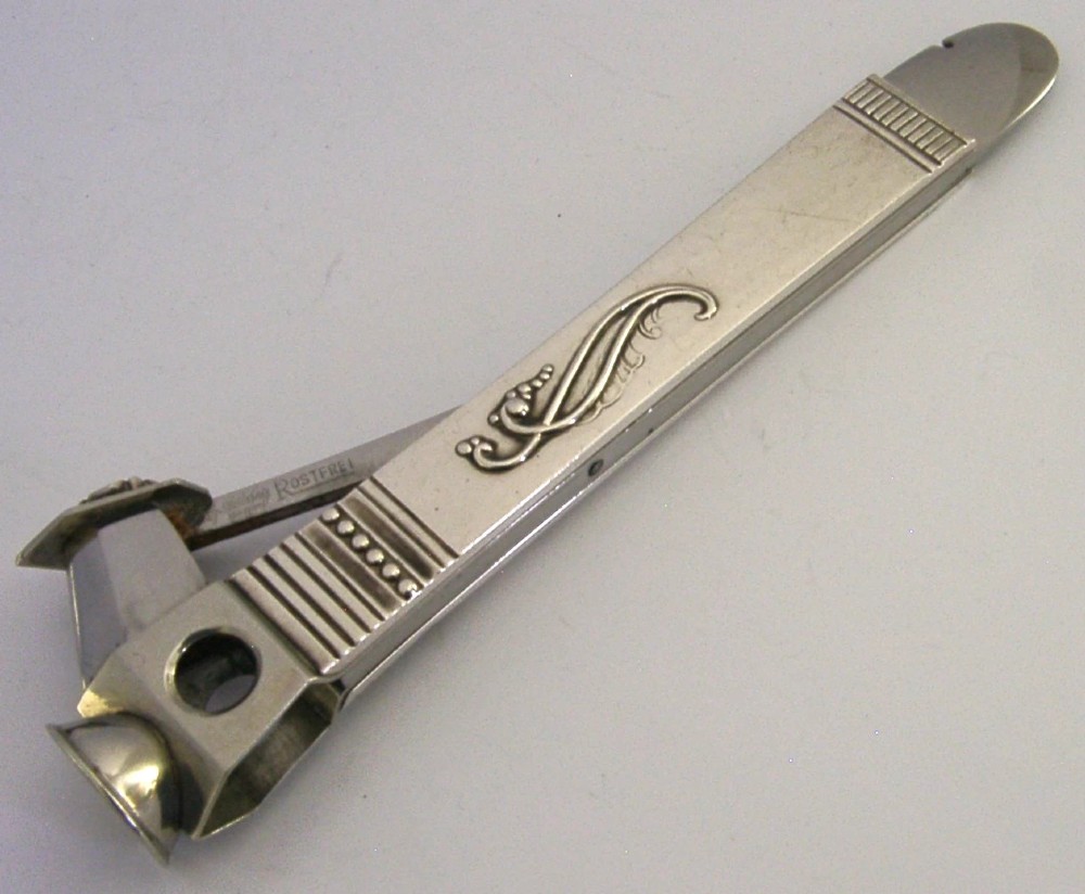 A mid-century sterling silver cigar cutter featuring a textured casing with a raised scroll motif and a stainless steel cutting blade.