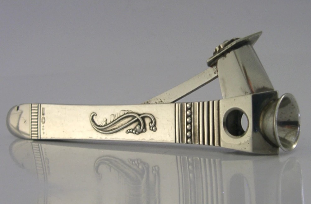 A mid-century sterling silver cigar cutter featuring a textured casing with a raised scroll motif and a stainless steel cutting blade. View V