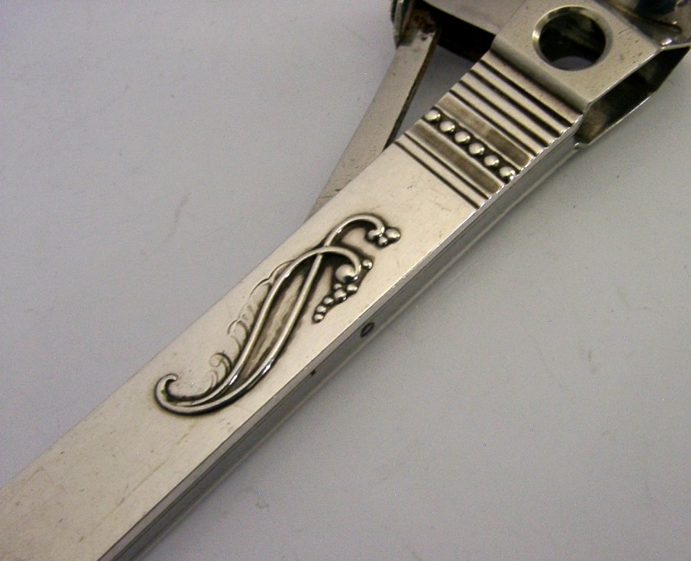 A mid-century sterling silver cigar cutter featuring a textured casing with a raised scroll motif and a stainless steel cutting blade. View VI
