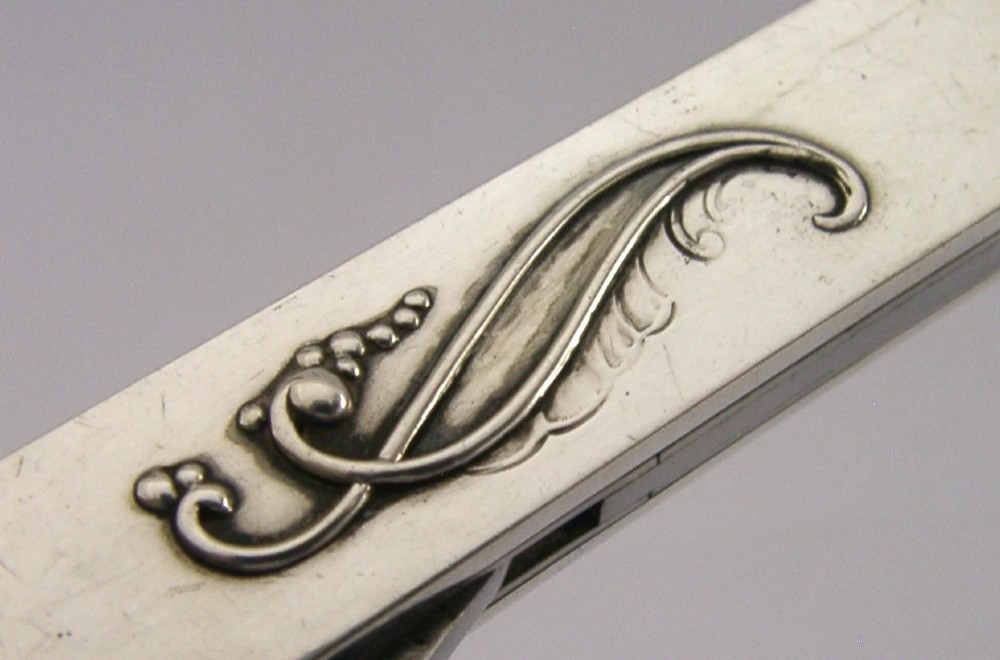 A mid-century sterling silver cigar cutter featuring a textured casing with a raised scroll motif and a stainless steel cutting blade. View IX