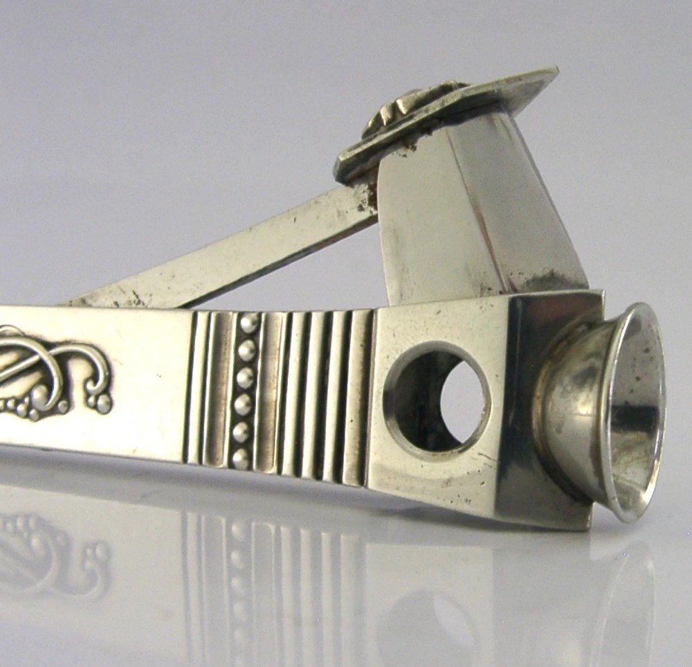 A mid-century sterling silver cigar cutter featuring a textured casing with a raised scroll motif and a stainless steel cutting blade. View X
