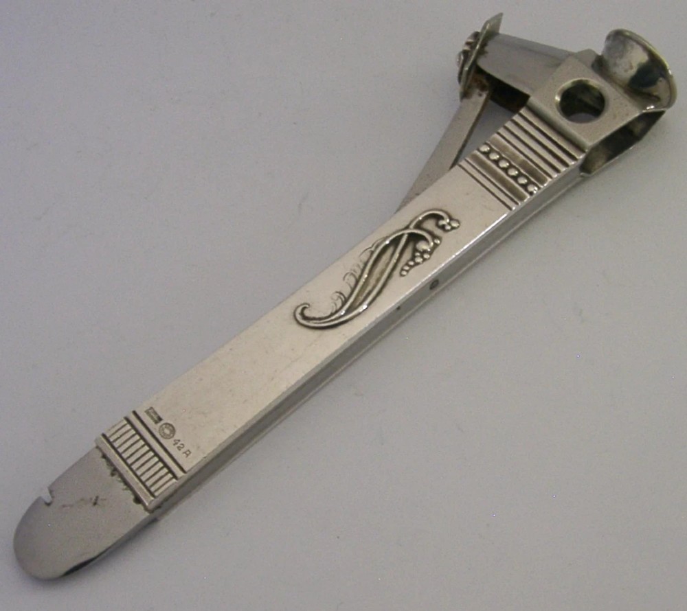 A mid-century sterling silver cigar cutter featuring a textured casing with a raised scroll motif and a stainless steel cutting blade. View XI