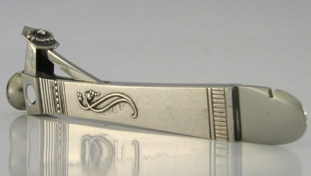 A mid-century sterling silver cigar cutter featuring a textured casing with a raised scroll motif and a stainless steel cutting blade. View XII