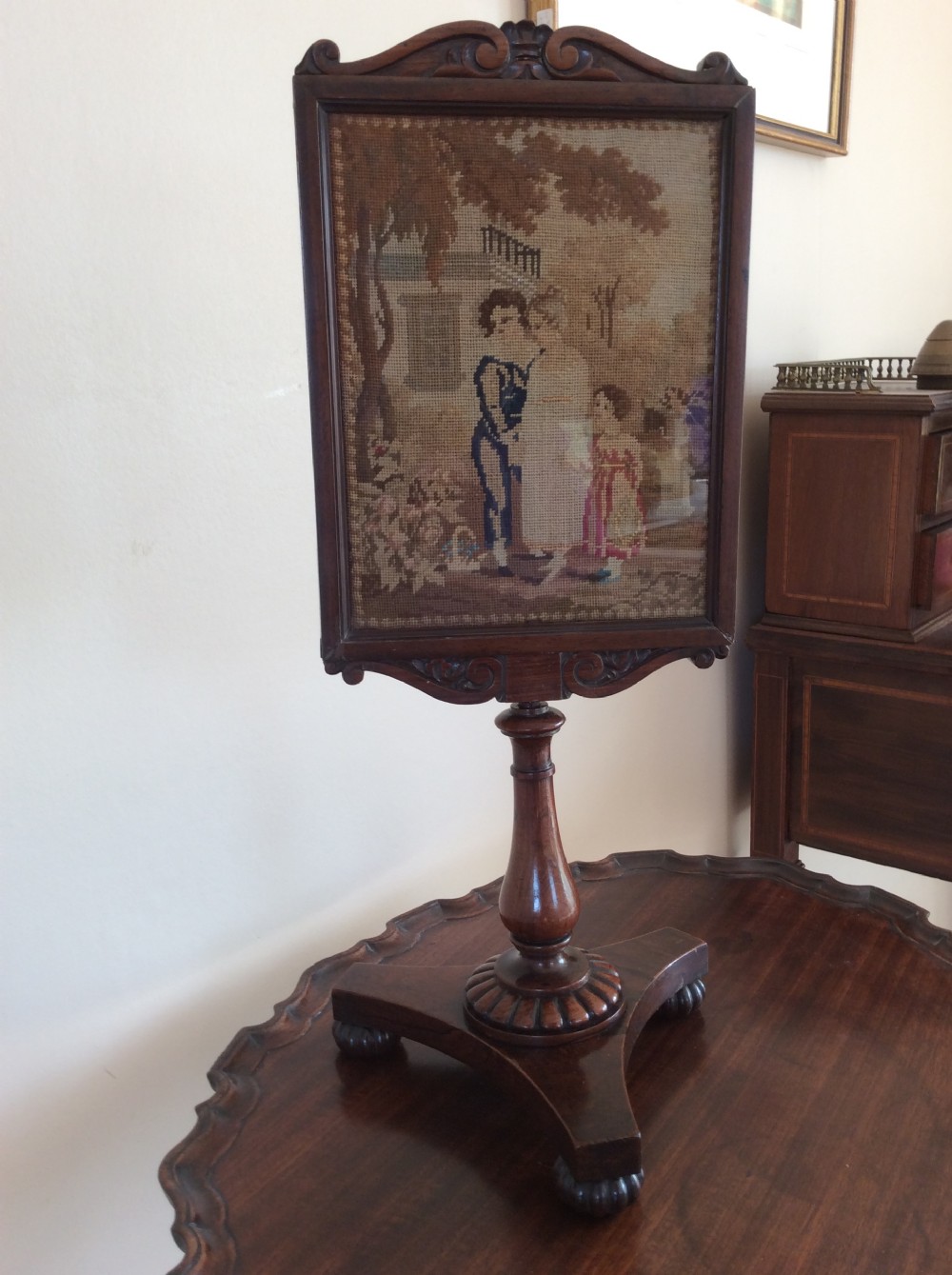 A William IV rosewood table face screen featuring a carved wooden frame with a framed needlework scene on a turned pedestal base. View VII