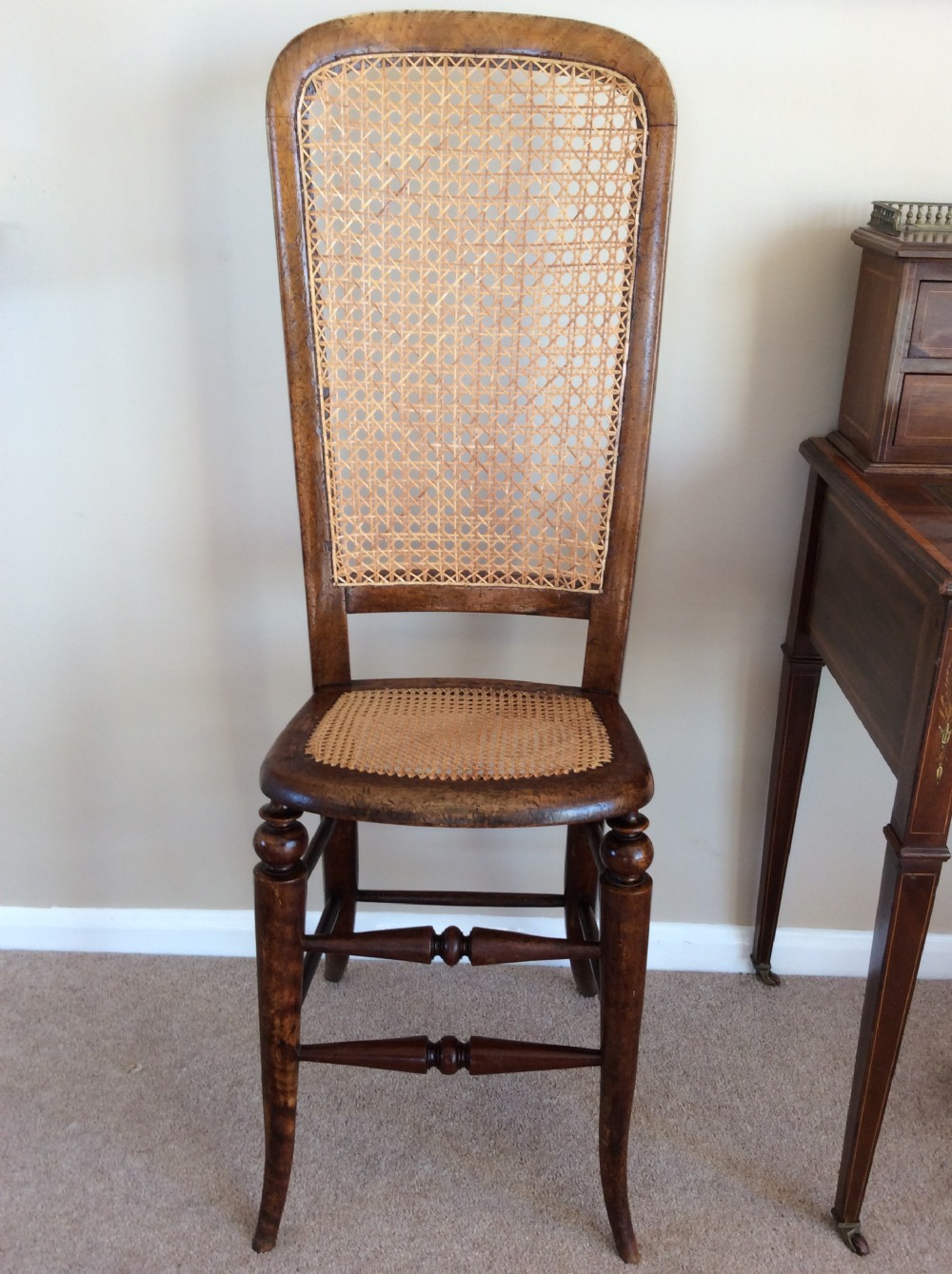 A Victorian wooden correction chair featuring an elongated backrest with woven cane panelling, a cane seat, and turned legs with central stretchers.