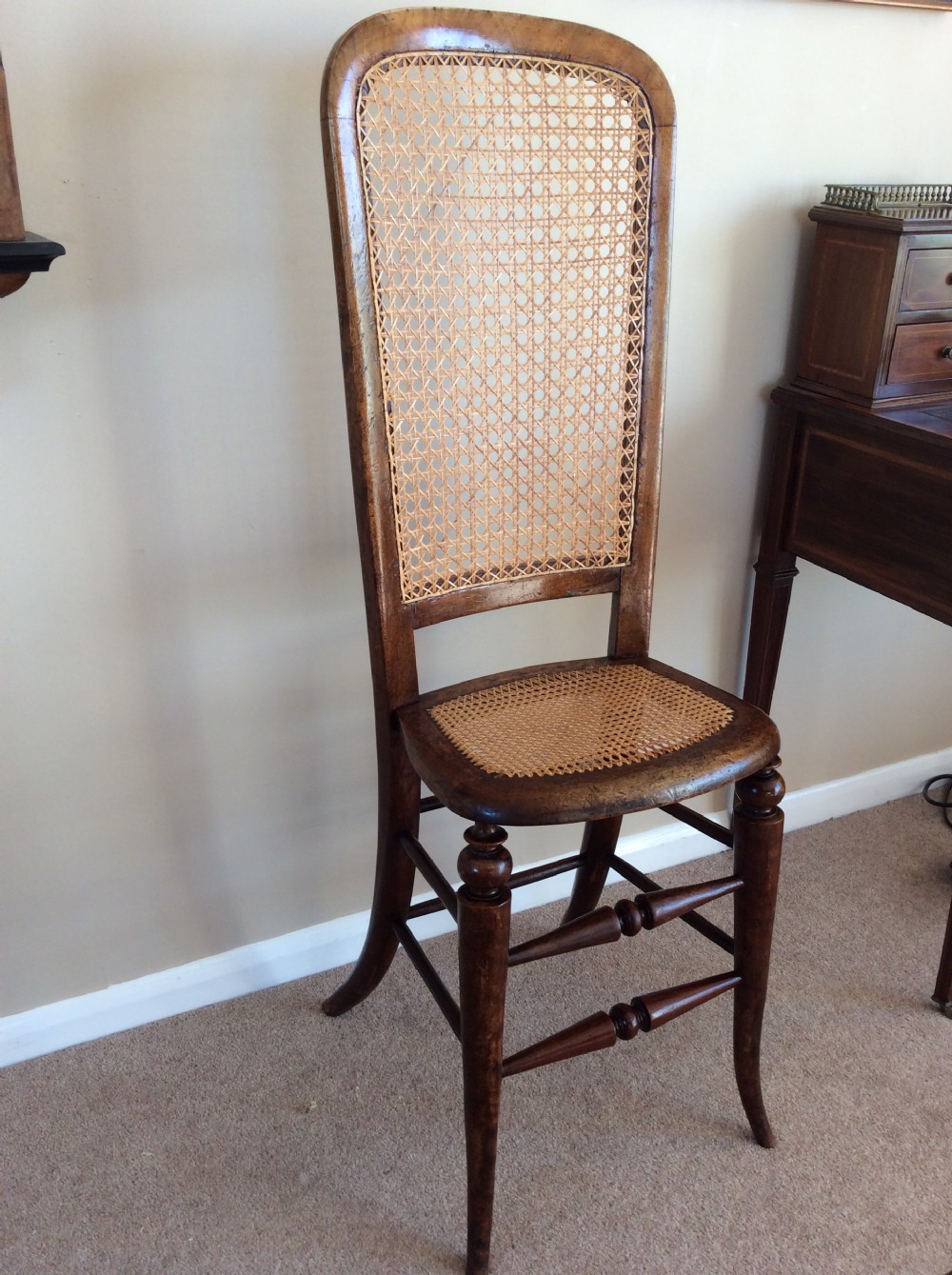 A Victorian wooden correction chair featuring an elongated backrest with woven cane panelling, a cane seat, and turned legs with central stretchers. View II