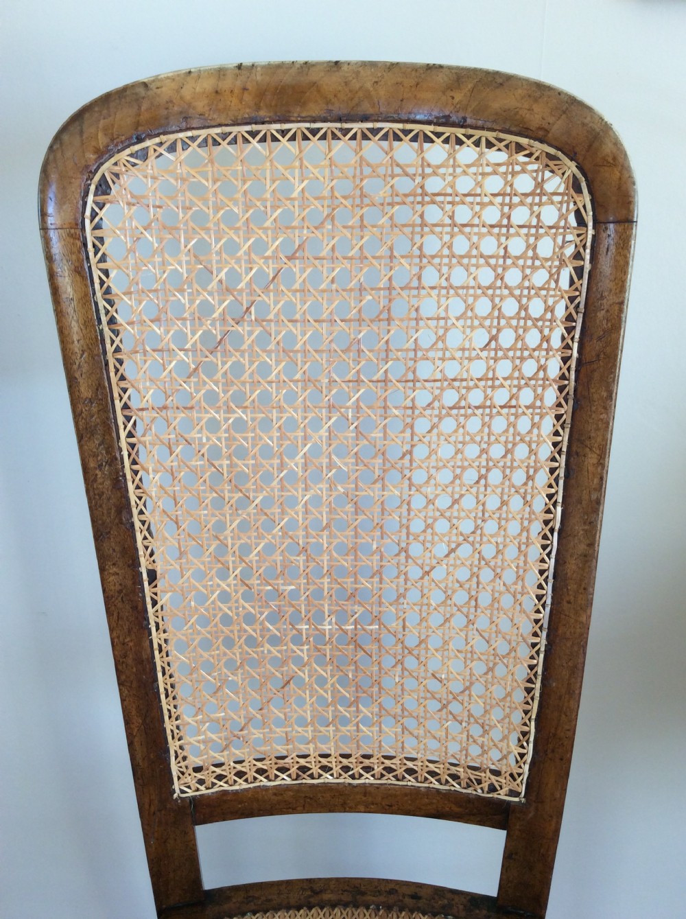 A Victorian wooden correction chair featuring an elongated backrest with woven cane panelling, a cane seat, and turned legs with central stretchers. View III
