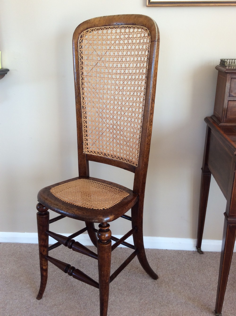 A Victorian wooden correction chair featuring an elongated backrest with woven cane panelling, a cane seat, and turned legs with central stretchers. View IV