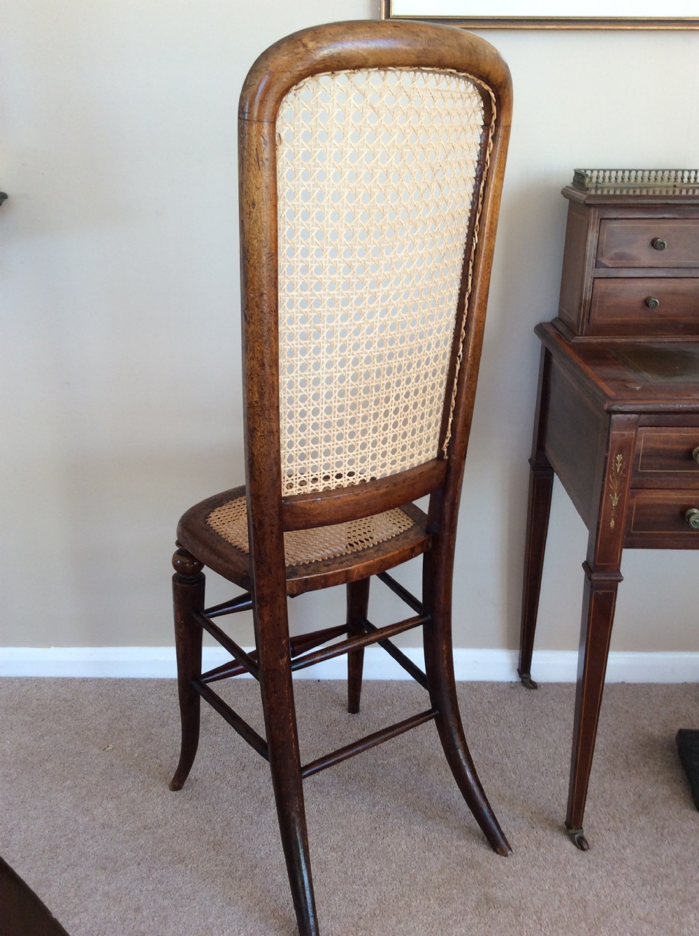 A Victorian wooden correction chair featuring an elongated backrest with woven cane panelling, a cane seat, and turned legs with central stretchers. View V