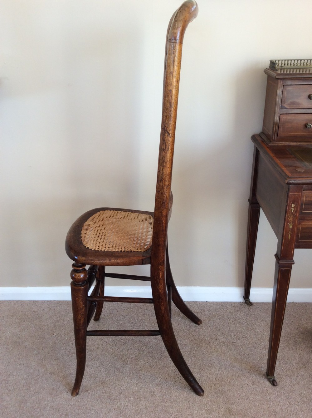 A Victorian wooden correction chair featuring an elongated backrest with woven cane panelling, a cane seat, and turned legs with central stretchers. View VI