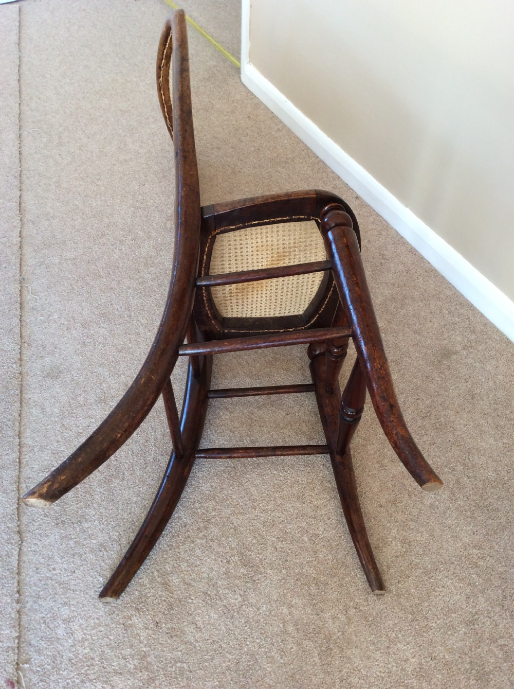 A Victorian wooden correction chair featuring an elongated backrest with woven cane panelling, a cane seat, and turned legs with central stretchers. View VII