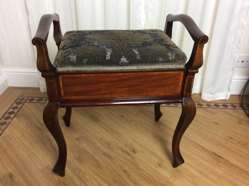 An Edwardian mahogany piano stool with raised side handles, satinwood line inlay, cabriole legs, and a dark patterned velvet upholstered seat.